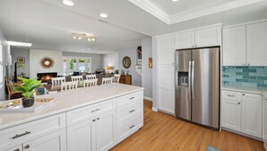 Una cocina moderna con armarios blancos, una isla grande, electrodomésticos de acero inoxidable y una zona de comedor con chimenea.