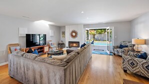 Una sala de estar moderna con un sofá modular, un televisor de pantalla plana, una chimenea y vista a una piscina.