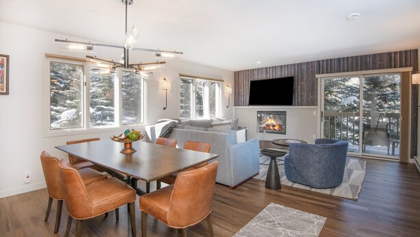 A modern living room with a fireplace, a dining area, and large windows with a view of snow-covered trees. - Ski-In and Out in Beaver Creek Village Condo w/ Balcony, Hot Tub, Free Shuttle  (Beaver Creek)