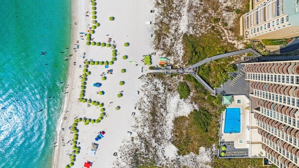 En vy över en strand sedd från luften, med en swimmingpool och en hotellbyggnad.