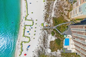 An aerial view of a beach with a swimming pool and a hotel building.