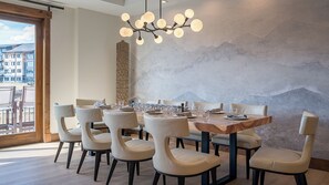 A dining area with a large table set for six, surrounded by six chairs, a modern chandelier, and a textured wall.