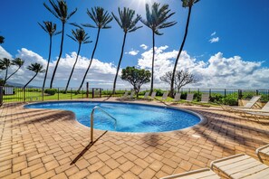 Ein Pool mit Ziegelterrasse, umgeben von Palmen und Liegestühlen.