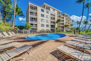A hotel with a swimming pool, lounge chairs, and palm trees. - Kihei Beach #306 – Unwind with Unmatched Ocean Views (Kihei)