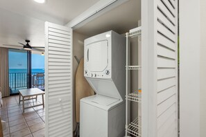 A laundry area with a washing machine and dryer, a table, and a view of the ocean through a sliding door.