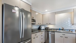 Une cuisine moderne dotée d’appareils électroménagers en acier inoxydable, de meubles de couleur claire et d’un revêtement mural en carreaux.