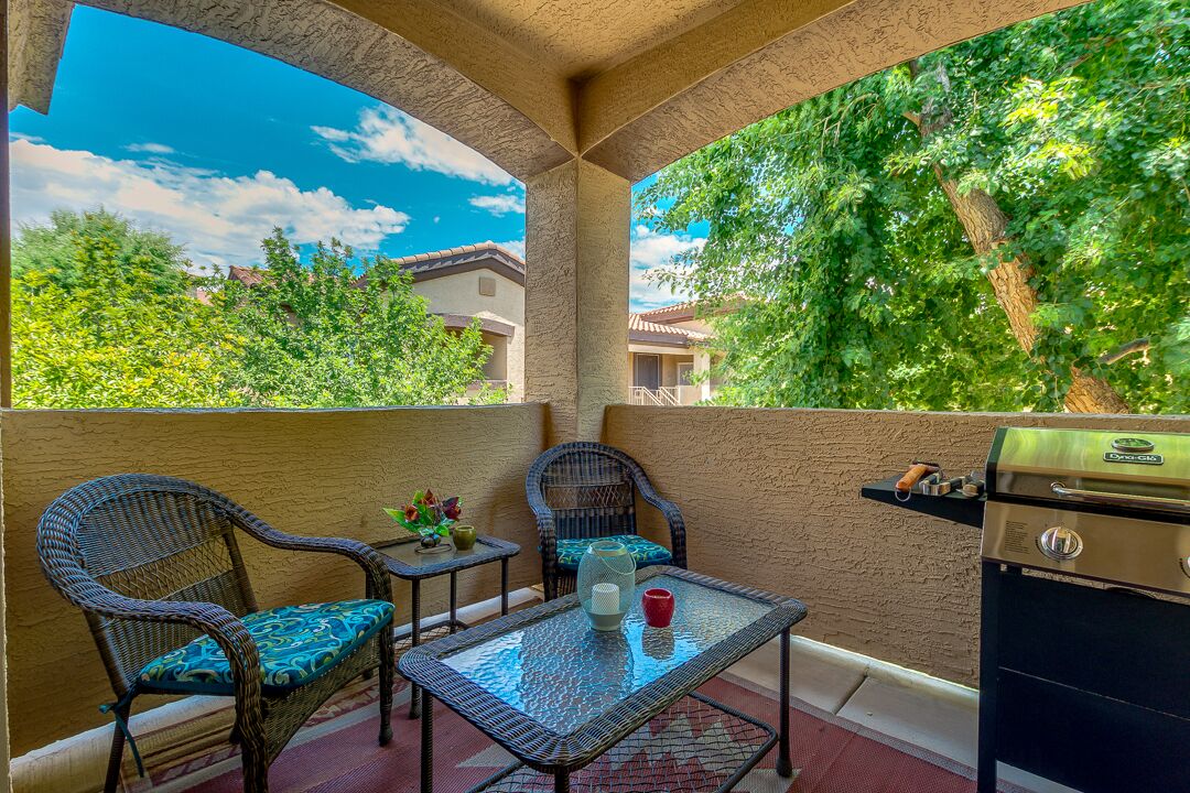 An outdoor patio with wicker chairs, a glass table, and a grill.