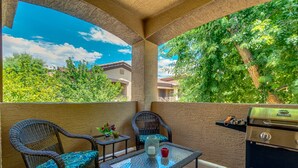 An outdoor patio with wicker chairs, a glass table, and a grill. - 2BR condo w community pool, hiking trails (Mesa)