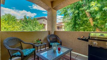 An outdoor patio with wicker chairs, a glass table, and a grill.