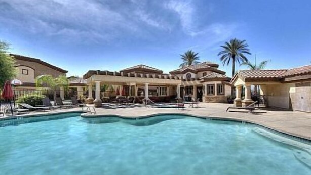 A swimming pool with lounge chairs and umbrellas, surrounded by buildings with Mediterranean architecture. - 2BR condo w community pool, hiking trails (Mesa)
