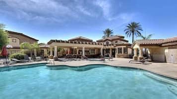 A swimming pool with lounge chairs and umbrellas, surrounded by buildings with Mediterranean architecture.
