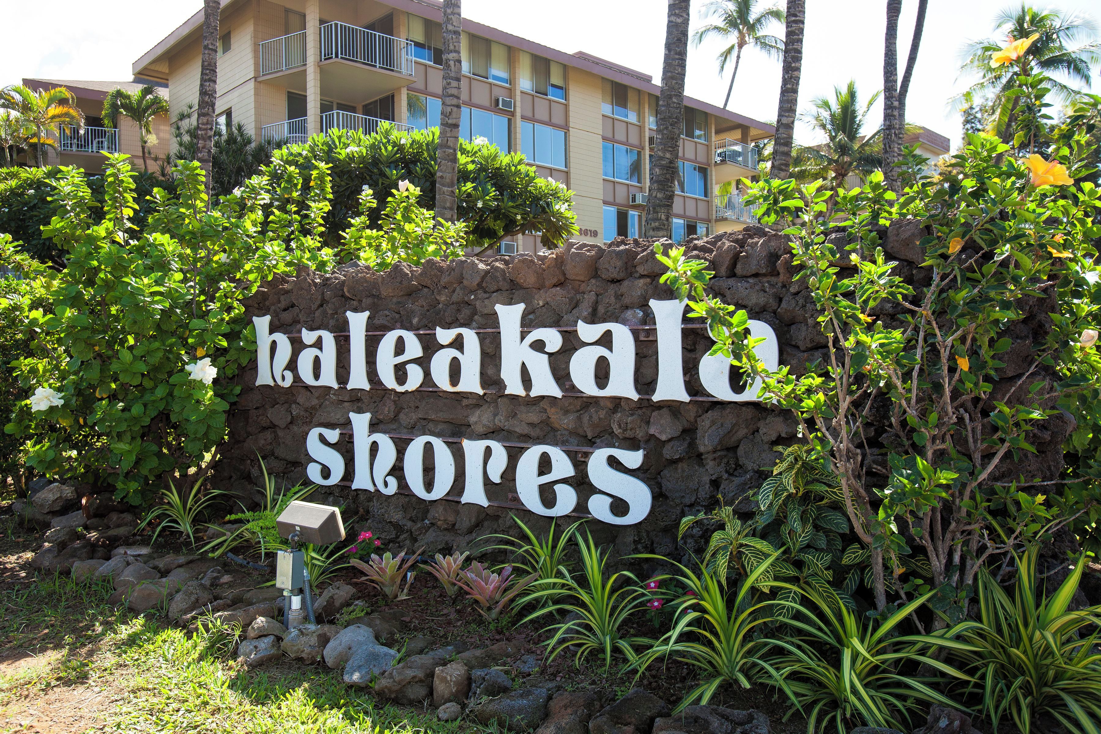 Een bordje voor 'Kaleakala Shores' met een stenen muur en tropische planten.