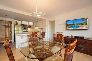 A modern kitchen with white cabinets, a glass dining table, and wooden chairs.