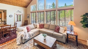 A cozy living room with a large sectional sofa, a wooden coffee table, and a dining area with a wooden table and chairs. - Unique Covered Silo Lounge | Fire-Pit Gatherings+ EV Ready & 1PM Check-IN/OUT (ronald)