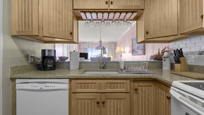 Une cuisine avec des meubles en bois, un lave-vaisselle, une machine à café, un évier et un luminaire suspendu.