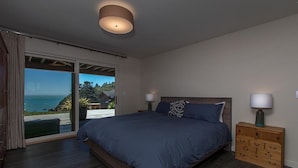 A bedroom with a large bed, a nightstand, a wooden dresser, and a view of the ocean through a sliding glass door. - Treasure Cove-Hot Tub, Ocean Views & Near Beach (Trinidad)