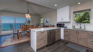 A modern kitchen with a large island, wooden cabinets, and a view of the sea. - Treasure Cove-Hot Tub, Ocean Views & Near Beach (Trinidad)