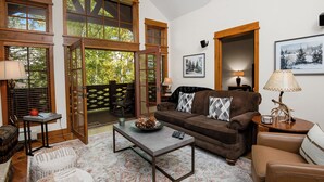 A cozy living room with a brown sofa, a coffee table, and a view of the outdoors through large windows. - Roomy, Luxurious Ski-In/Ski-Out w/ Views, Hot Tub! Bachelor Gulch, Beaver Creek (Edwards)