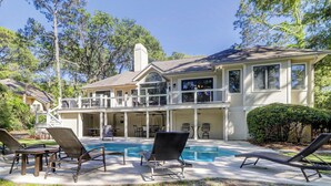 A two-story house with a pool, outdoor seating, and a covered patio area.