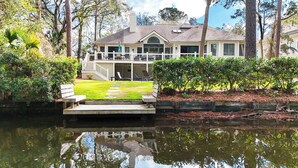 A house with a dock extending over a body of water, surrounded by lush greenery and trees.