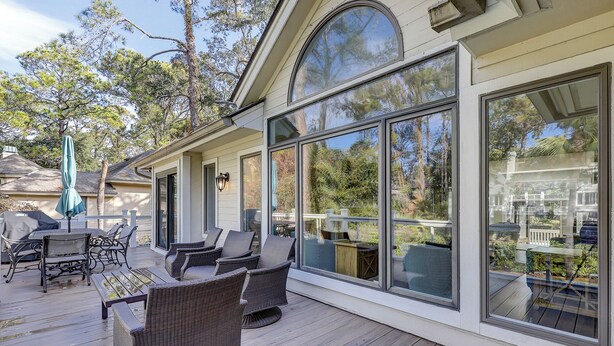 A covered patio with wicker furniture and a large glass door leading to a deck.