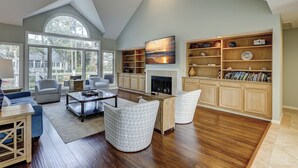 A spacious living room with a fireplace, wooden cabinets, and a large window offering a view of the outdoors.