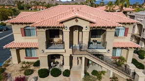 A two-story building with a red-tiled roof, balconies, and a staircase leading to the entrance.