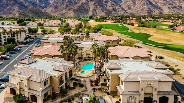 A residential area with multiple buildings, a swimming pool, and a golf course in the background.