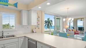 A kitchen with white cabinets, a dishwasher, and a view of the beach.