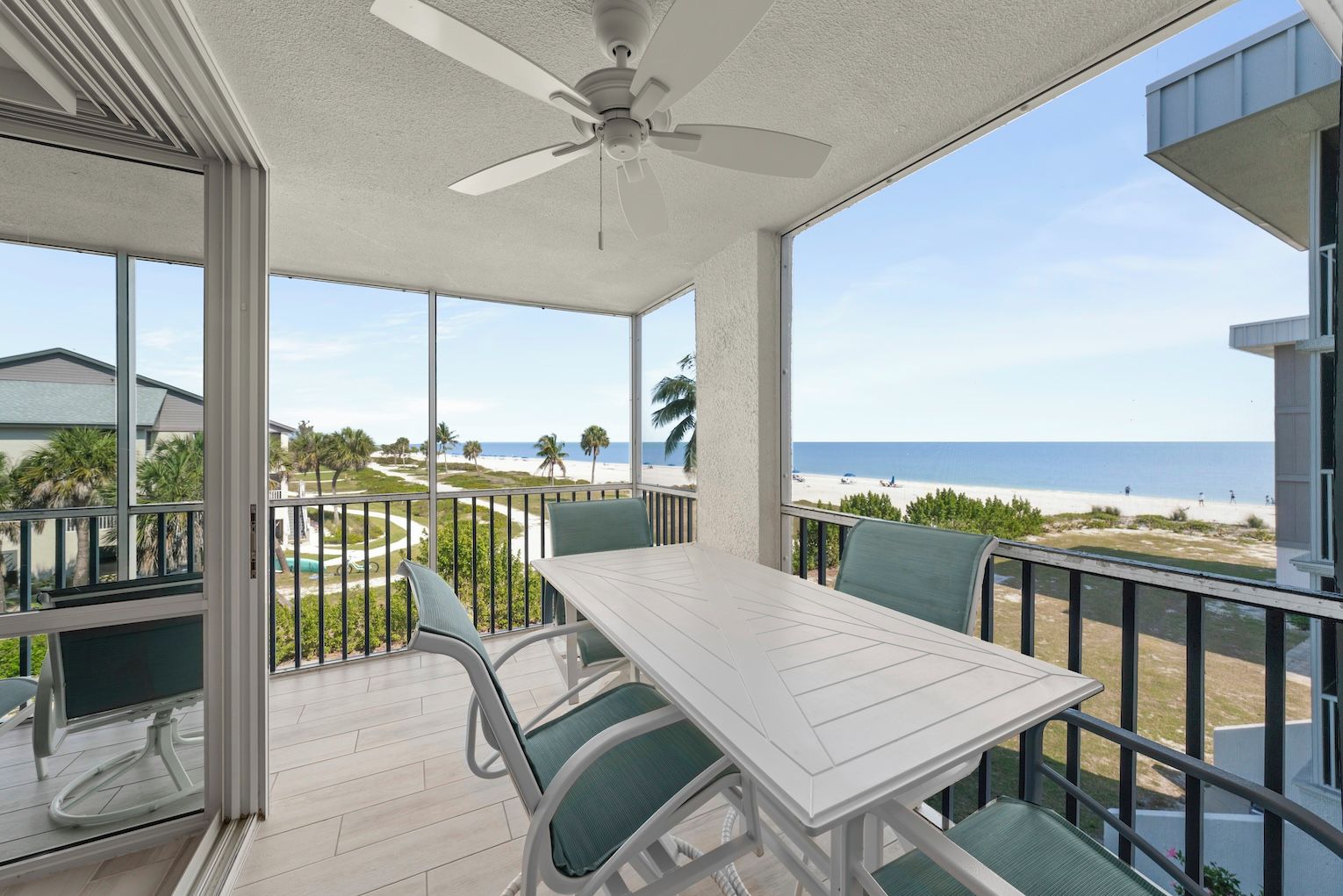 A balcony with a table and chairs, a ceiling fan, and a view of the beach.