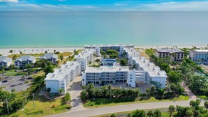 A beachfront hotel with multiple buildings, a parking area, and a view of the ocean.