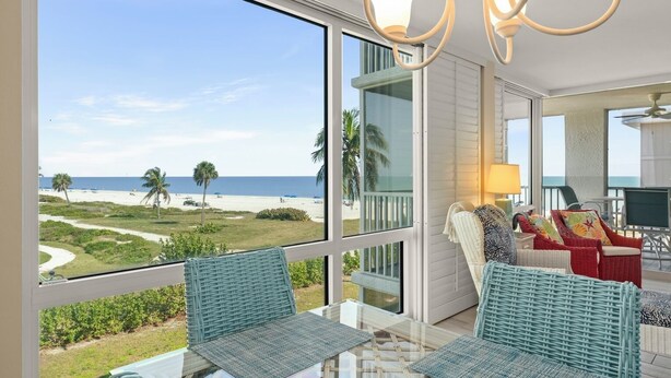 A room with a large window overlooking a beach, wicker furniture, and a ceiling fan.