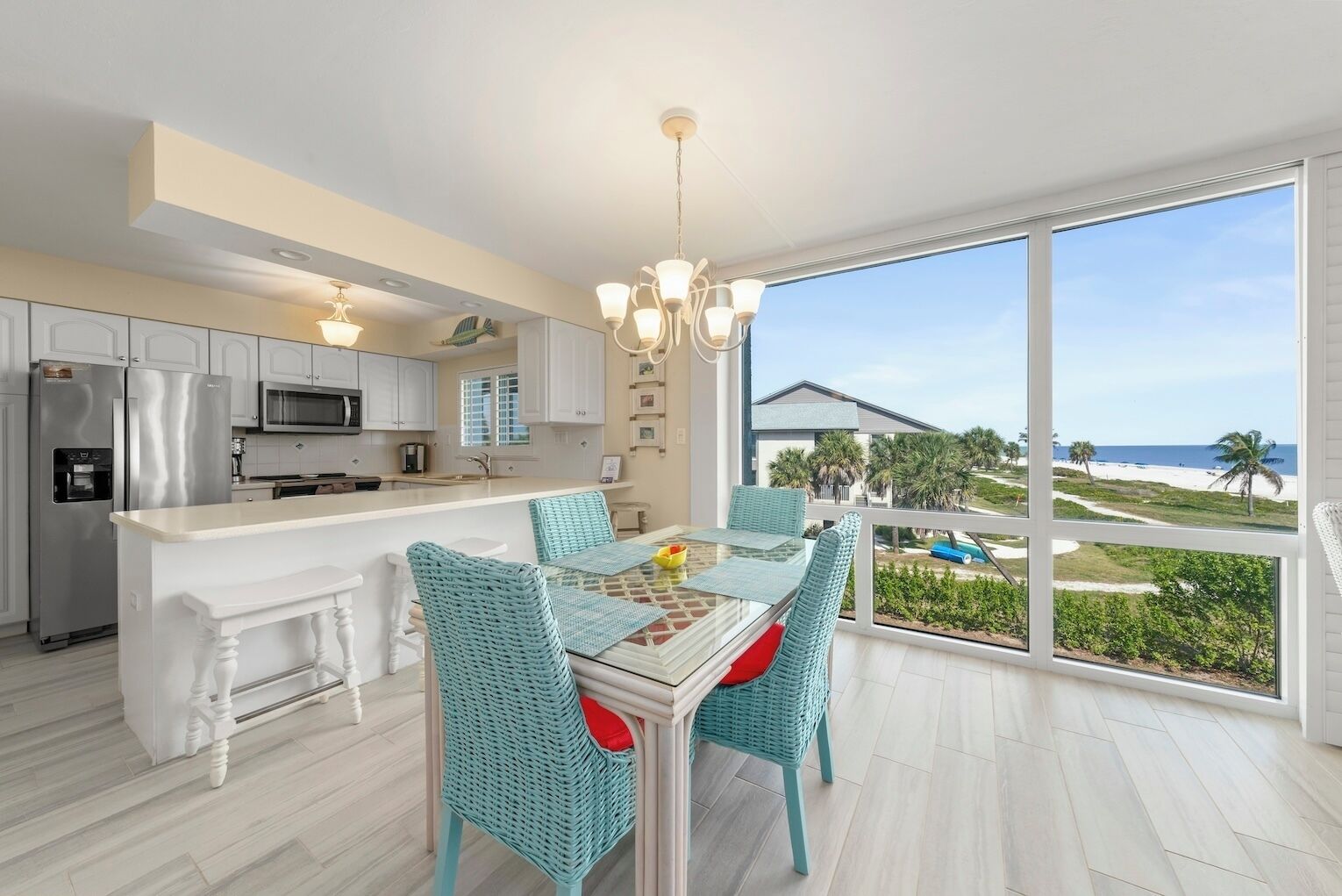 Een moderne keuken met witte kasten, roestvrijstalen apparatuur en een eethoek met een glazen tafel en rieten stoelen.