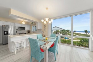 A modern kitchen with white cabinetry, stainless steel appliances, and a dining area with a glass table and wicker chairs. - Island Beach Club #330E is a 2/2 vacation rental on Sanibel Island! (Sanibel)