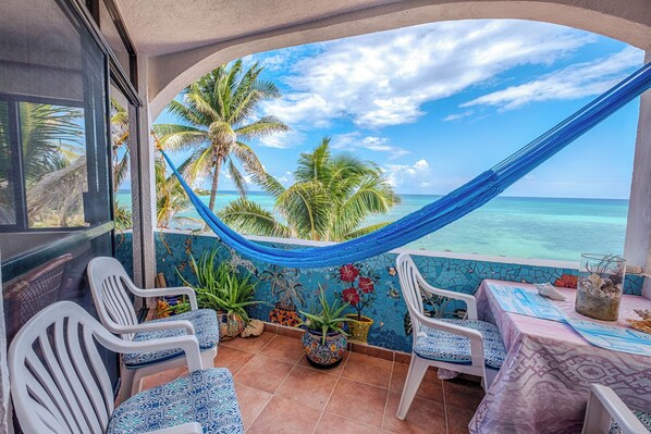 A balcony with a view of the ocean, a hammock, and potted plants.