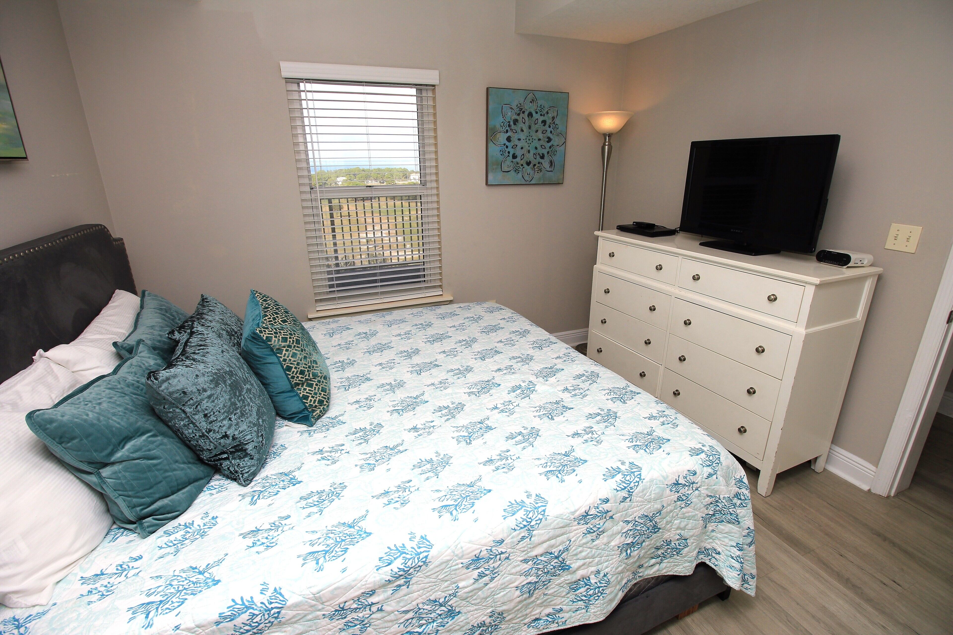 A bedroom with a bed, a dresser, a television, and a window with blinds.