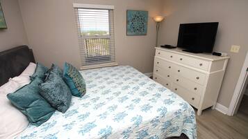 A bedroom with a bed, a dresser, a television, and a window with blinds.