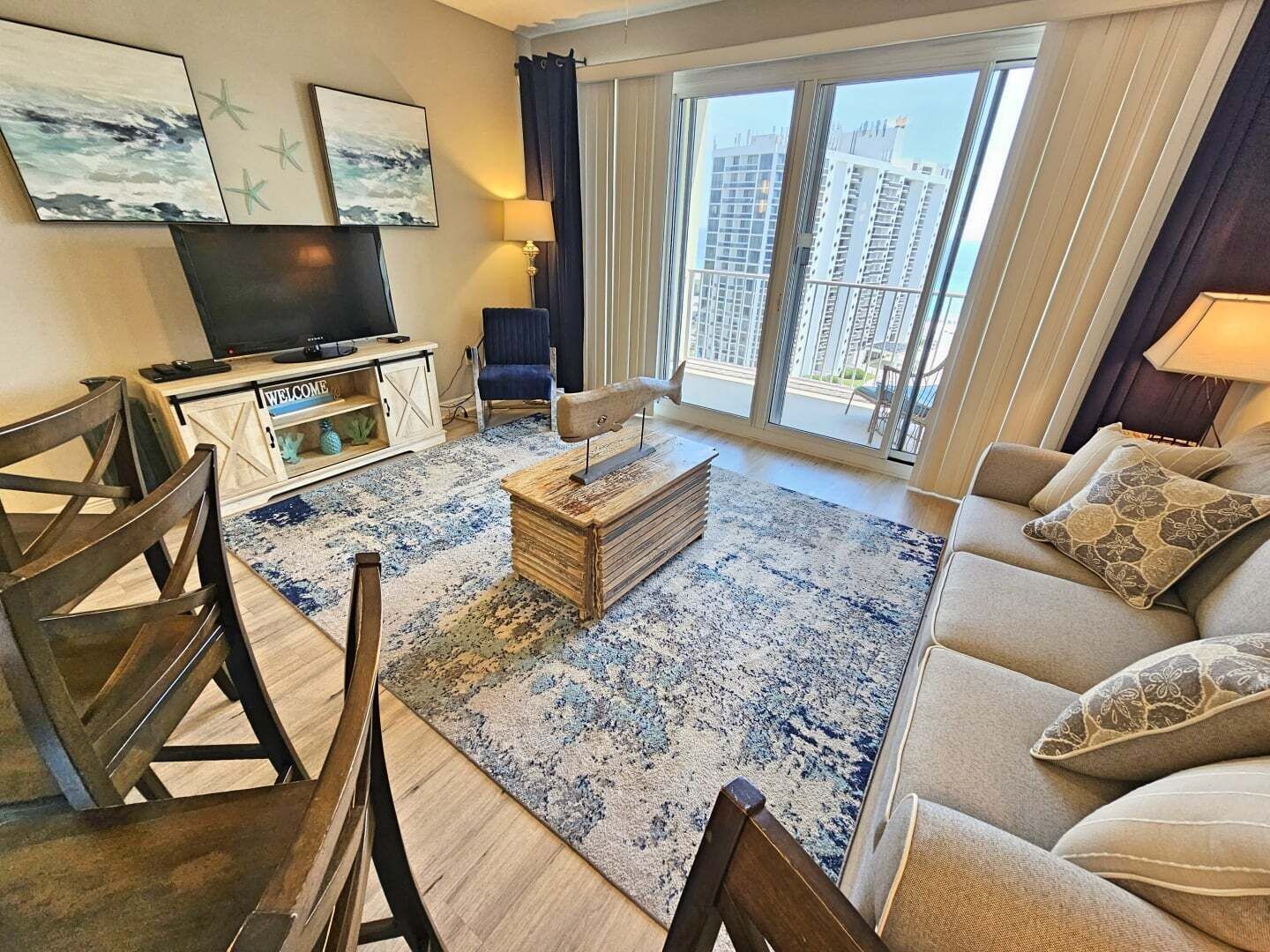 A modern living room with a television, a coffee table, and a sofa. There are two chairs and a window with a view of buildings.