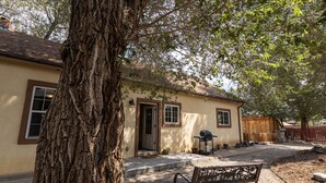 Una casa amb un gran arbre al davant, una banca i una barbacoa.