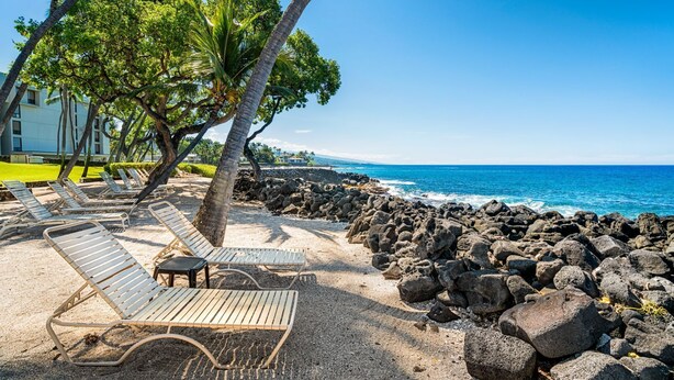 A beach with lounge chairs, a rocky shoreline, and a clear blue sky.