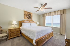 Ein Schlafzimmer mit Bett, Nachttischen, einem Sessel, einem Deckenventilator und einem Fenster mit Vorhängen.