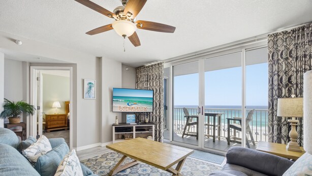Ein Wohnzimmer mit Fernseher, Sofa, Couchtisch und einem Balkon mit Blick auf den Strand.