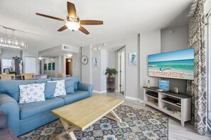 Un salon avec un canapé bleu, une table basse en bois et un téléviseur diffusant une émission intitulée « Legacy Vacations ».