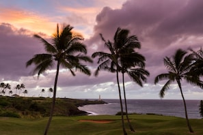 Un parcours de golf bordé de palmiers, avec un phare visible au loin.