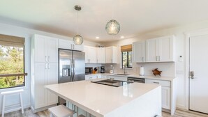 A modern kitchen with white cabinetry, stainless steel appliances, and a large island with bar stools. - Pono Kai A-201  Air conditioned,  Oceanfront Condo on the Coconut Coast (Kapaa)