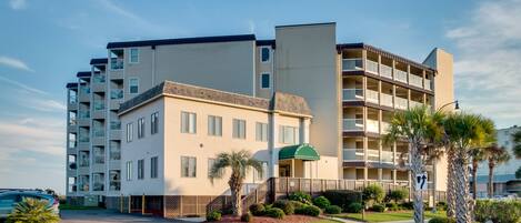 A multi-story hotel with balconies, a green awning, and a parking area.