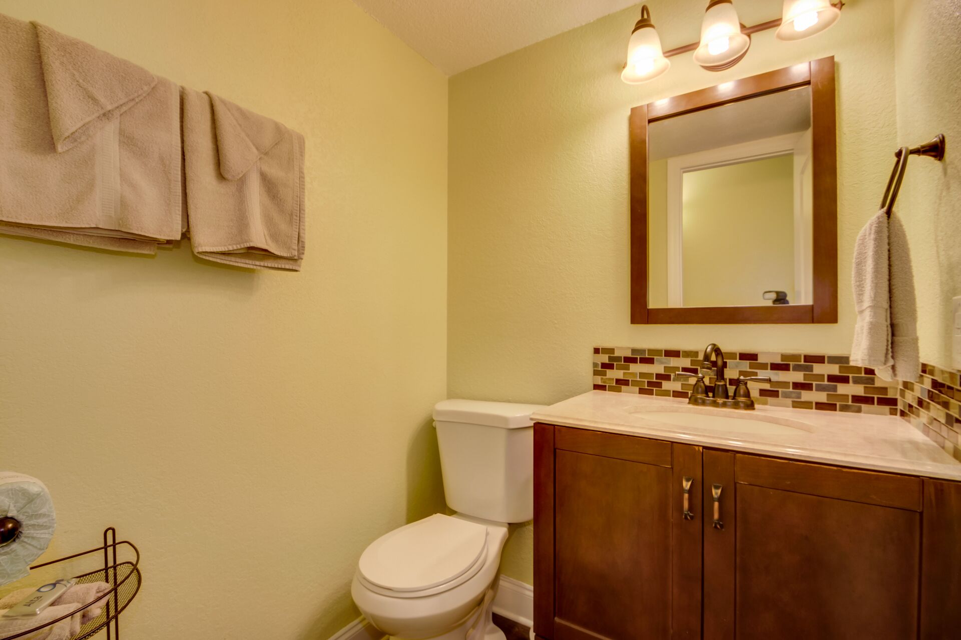 A bathroom with a toilet, sink, and mirror. There are towels hanging on the wall.