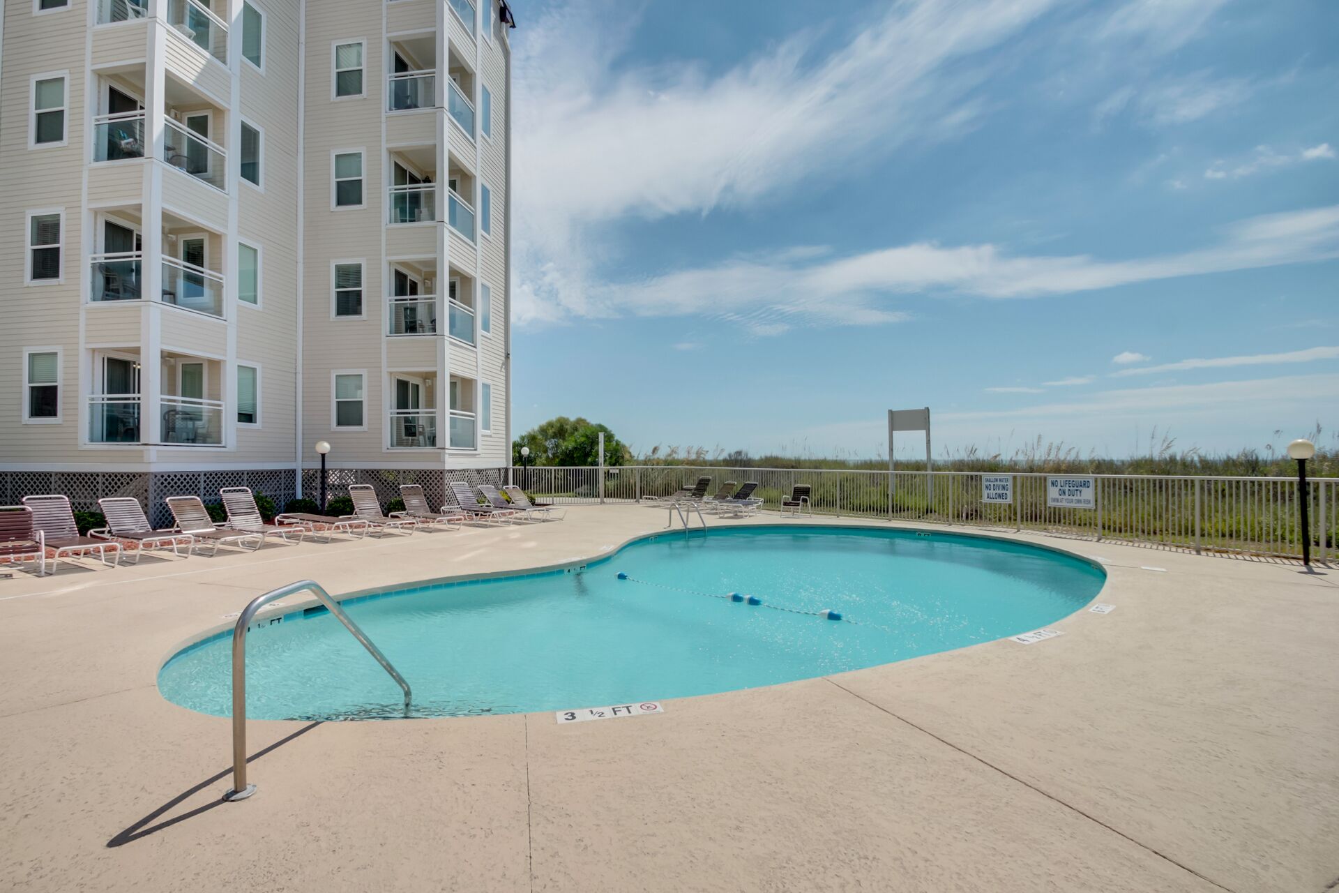 Une piscine avec des chaises longues et un bâtiment doté de nombreux balcons.
