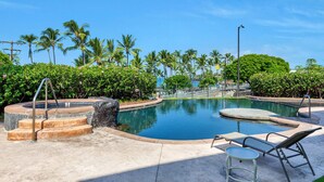 A pool area with lounge chairs and a hot tub, surrounded by palm trees and a clear sky.