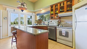 A kitchen with a central island, stainless steel appliances, wooden cabinets, and a view of palm trees outside.
